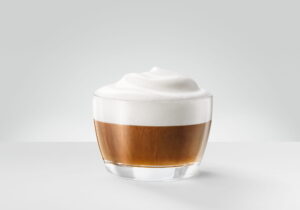 A cappuccino in a wide cup under a tall dome of dense white milk foam