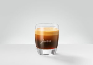 A single espresso in a small glass tumbler, dark coffee beneath a fine hazelnut crema