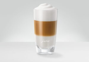 A latte macchiato in a tall glass showing three distinct layers of milk, coffee and white foam