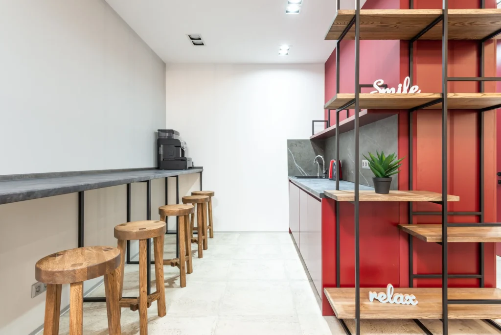 A modern office kitchenette with a bean-to-cup coffee machine on the counter and stools along a breakfast bar