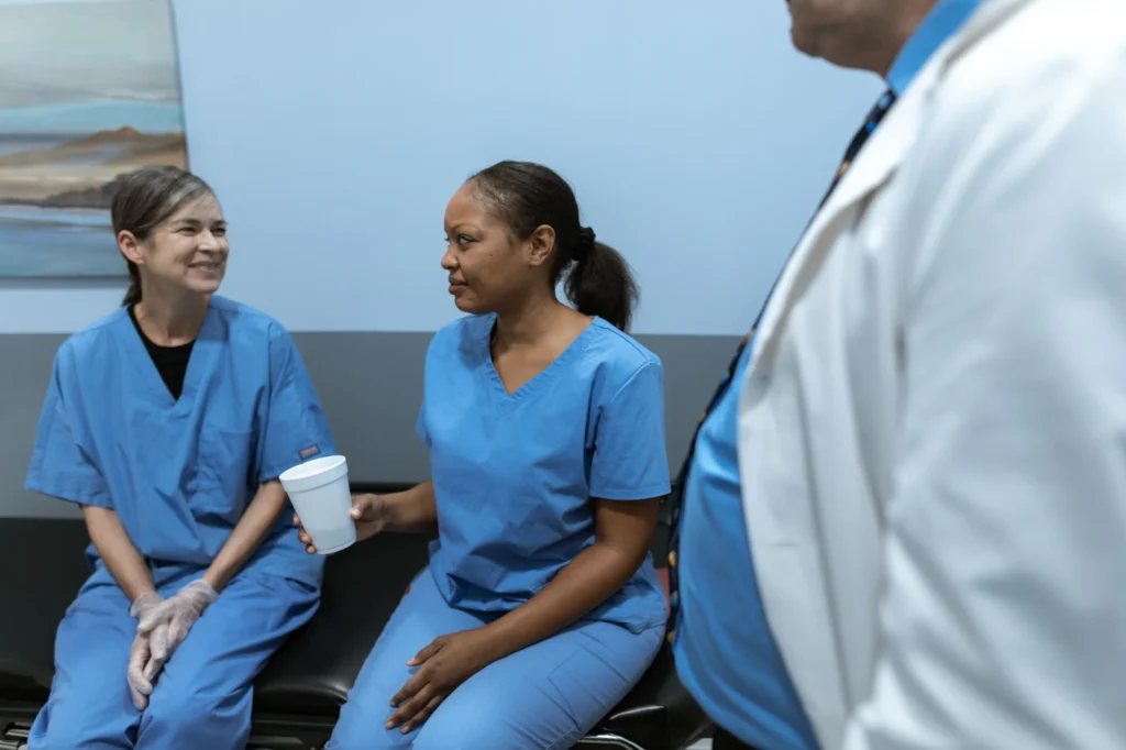 Two members of clinical staff in scrubs taking a coffee break together, one holding a cup