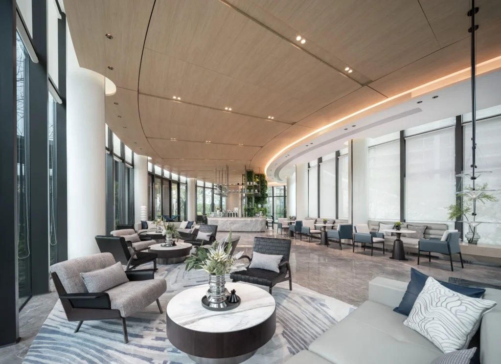 A hotel lounge with a curved timber ceiling, armchairs and floor-to-ceiling glass