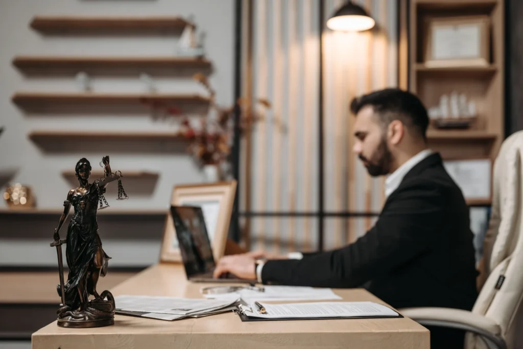 An attorney working at a desk in a wood-panelled law office, a bronze scales-of-justice figure in the foreground