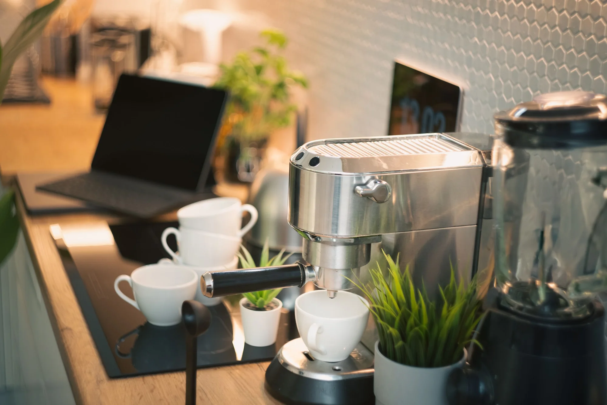 An espresso machine, white cups and a laptop on an office coffee bar
