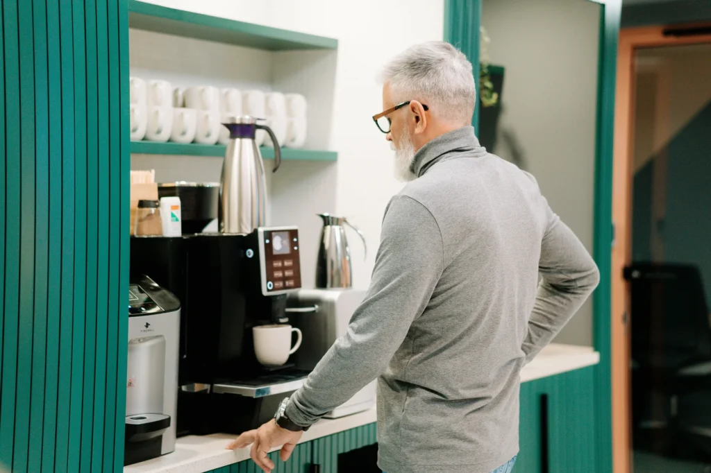 A colleague serving himself coffee at an office coffee station with a bean-to-cup machine and carafes